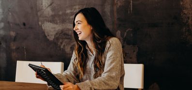 A woman laughs while looking off to her right and holding a tablet