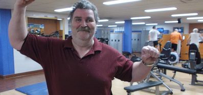 An image of John Black in a YMCA gym raising his arms in celebration after losing 100 pounds