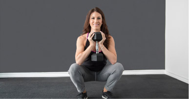 Woman in a squat position holding a dumbbell up to her chest