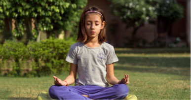 Young girl sits outside in a meditative pose with legs crossed and hands on knees