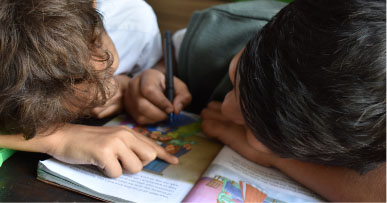 Young kids sit together looking at a book and colouring in it